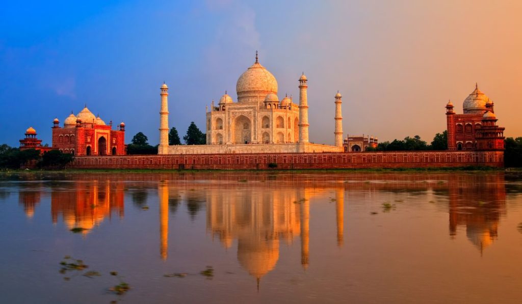 An empty view of the Taj Mahal at sunrise with no people, showing the monument's reflection in the calm water of the long pool.