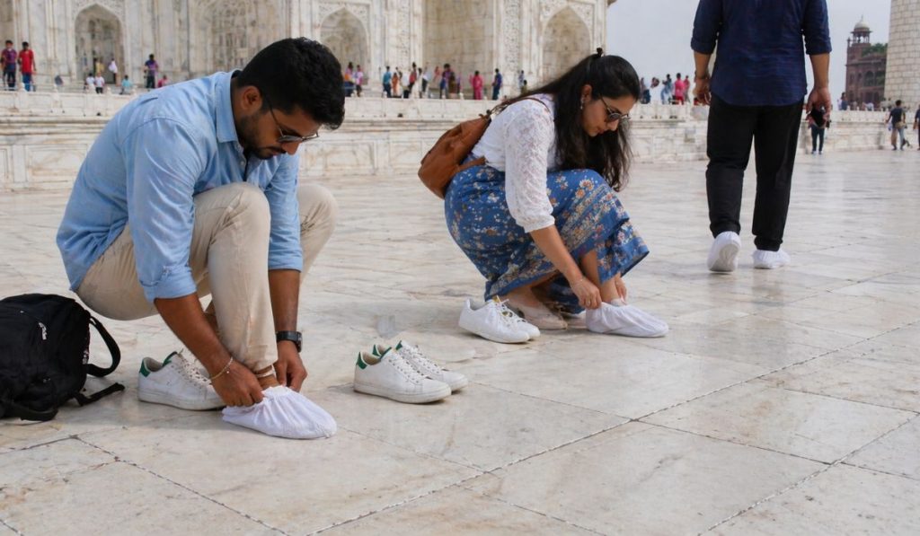 Tourists removing shoes and wearing shoe covers at Taj Mahal marble platform.